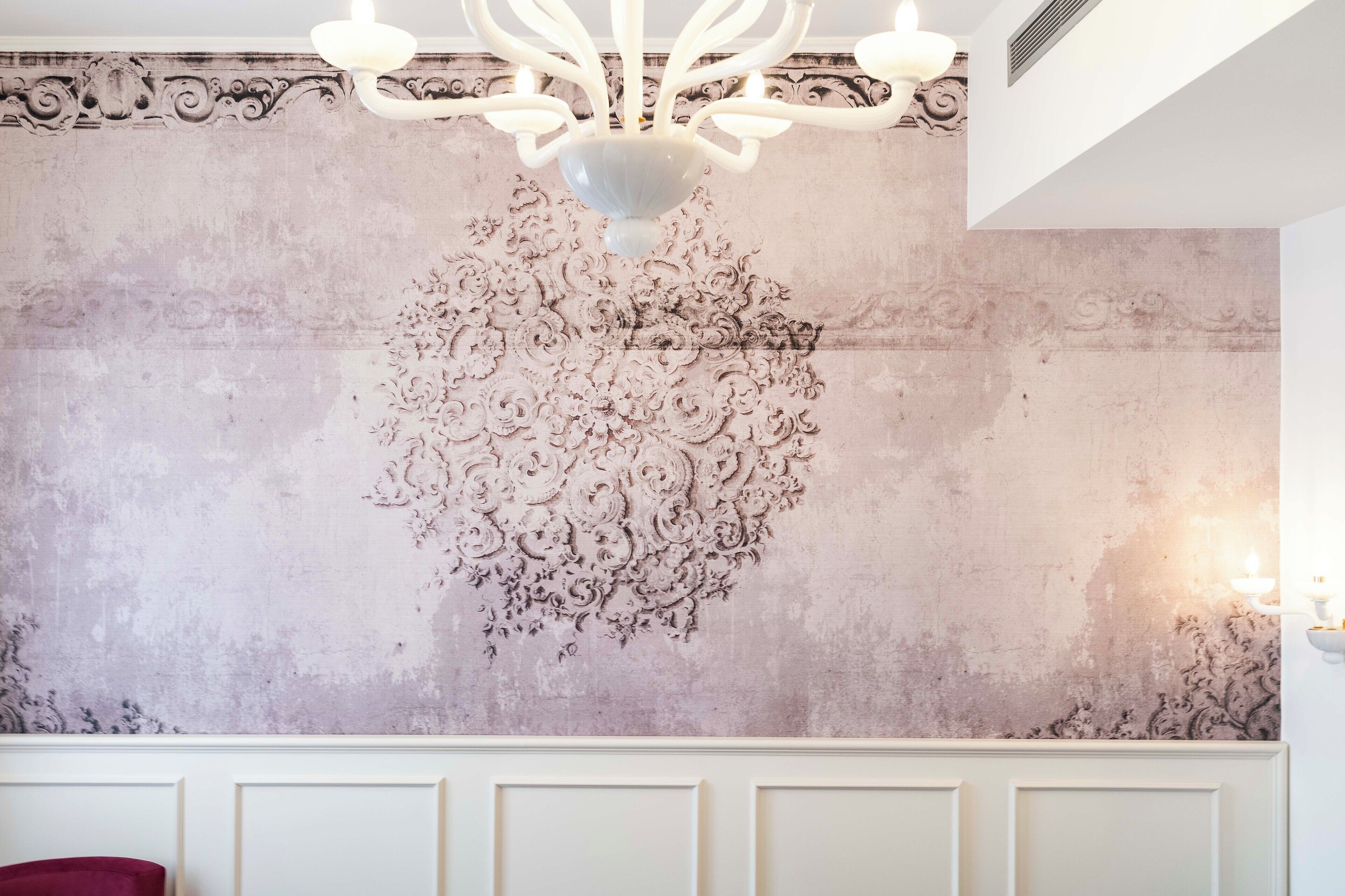 A room with a decorative wall, a chandelier, and a white panelled ceiling.