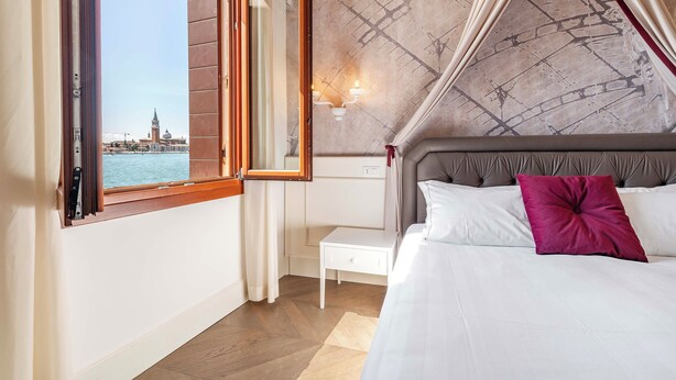 Un dormitorio con cama, mesita de noche, ventana con cortinas y vista a la ciudad.