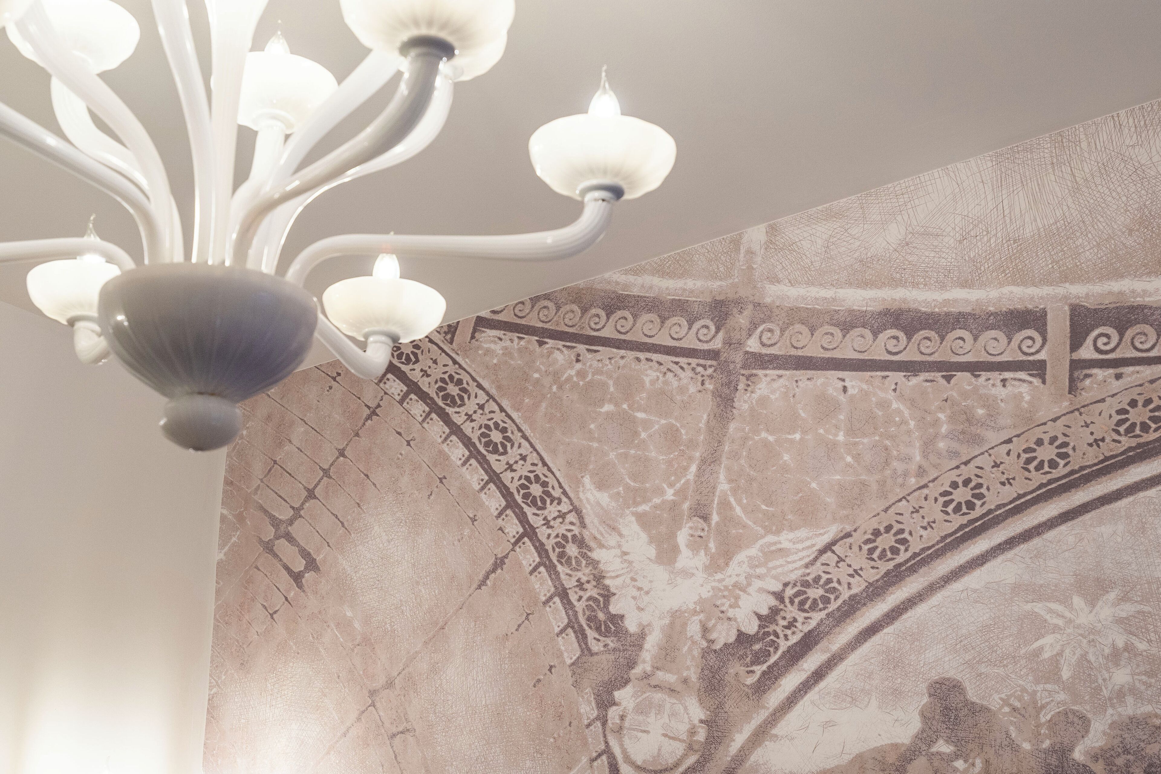 Ein Kronleuchter mit mehreren Armen und Leuchten, eine Wand mit Muster und geometrischem Design sowie eine strukturierte Oberfläche.