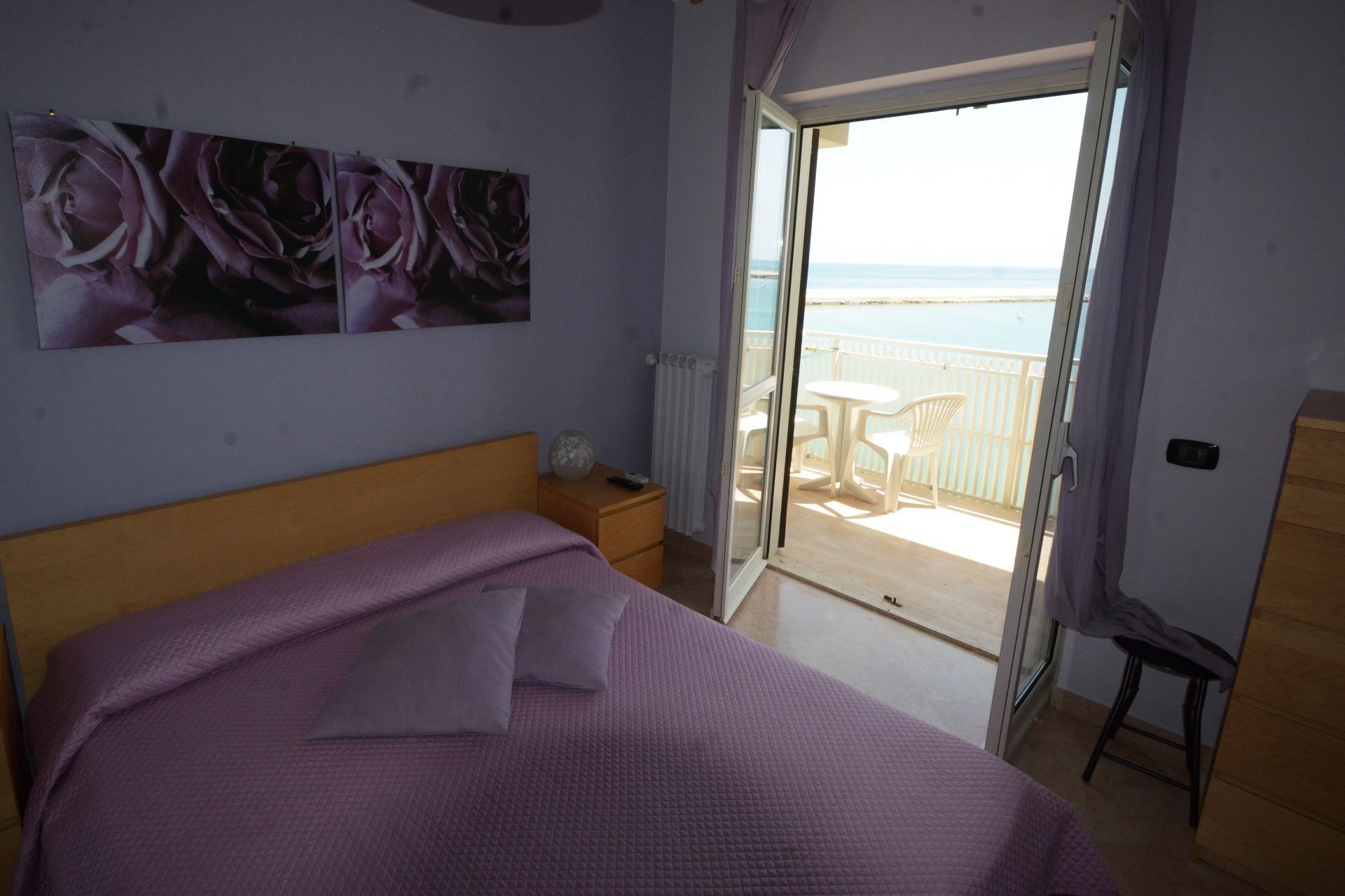 Une chambre à coucher avec un lit, une table de chevet, un tableau et une vue sur la mer par une porte ouverte.