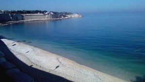 Vista costeira com mar azul cristalino, praia arenosa e falésias rochosas.