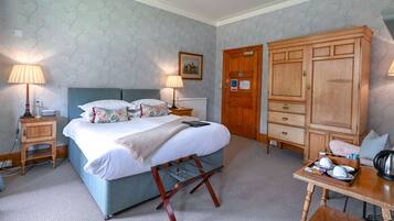 A bedroom with a bed, bedside lamps, a wooden wardrobe, a small table with cups and a kettle, and a radiator.