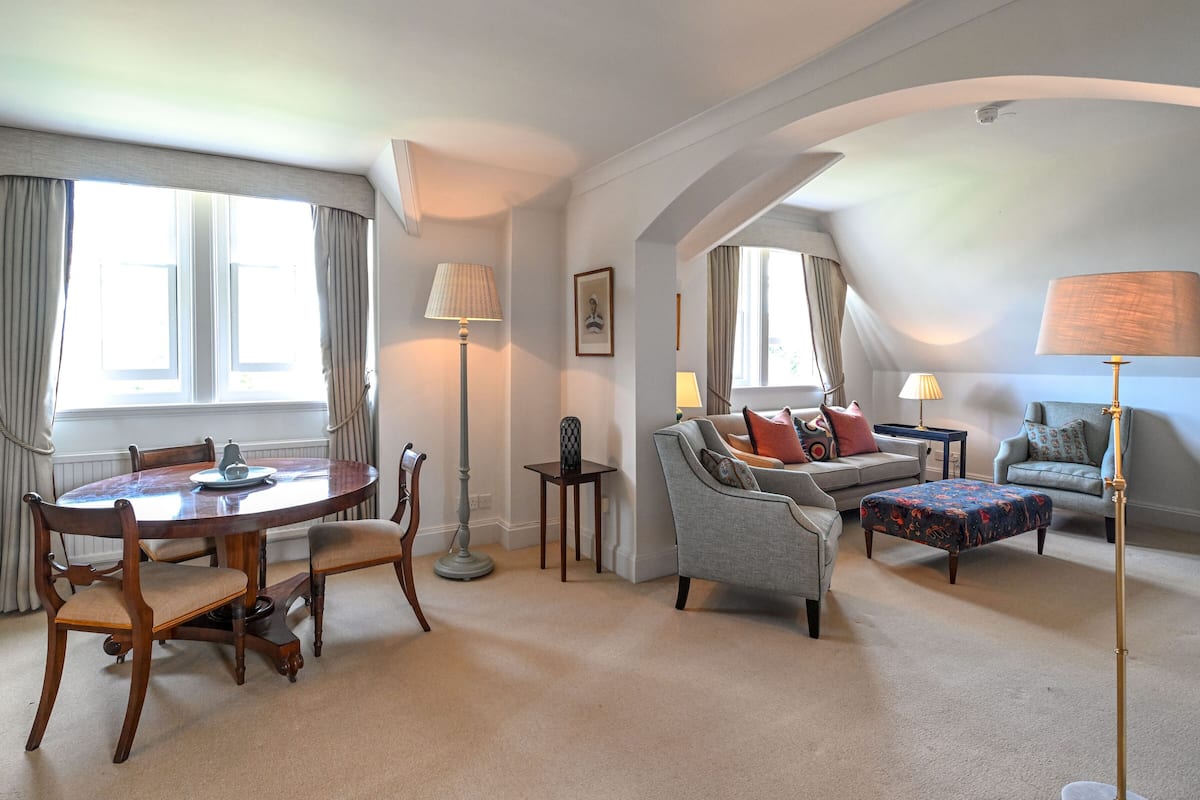A well-lit living room with a round wooden table, two sofas, and a floor lamp.