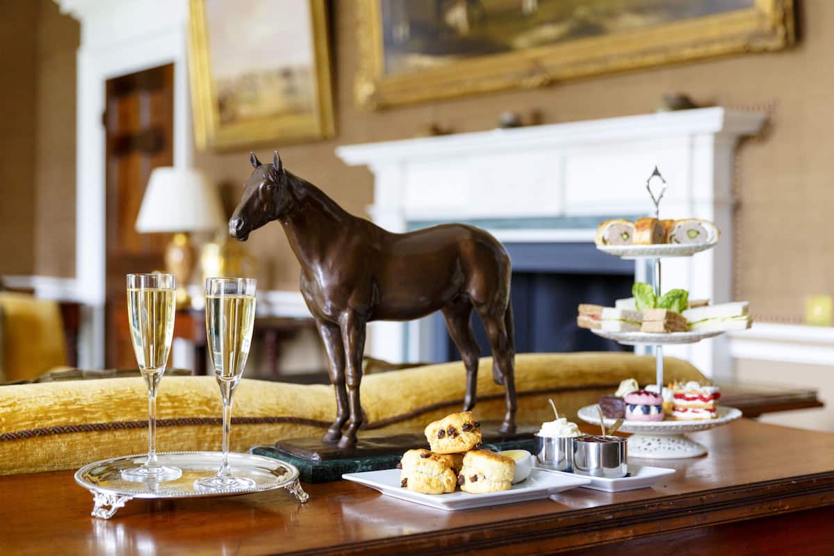 A dining table with a horse statue, champagne glasses, and a variety of pastries and sandwiches.