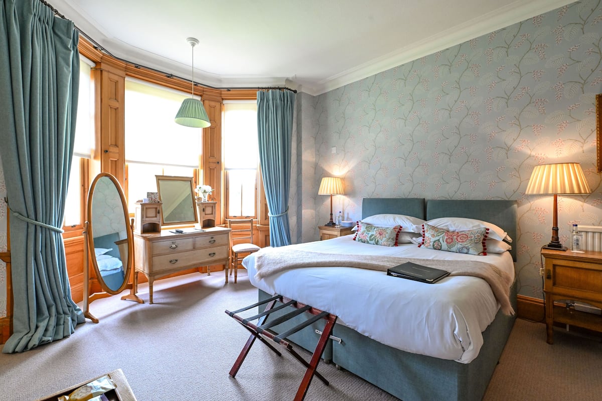 A bedroom with a bed, dresser, vanity, and two bedside lamps.