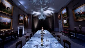 Un comedor formal con una larga mesa dispuesta para una comida, rodeada de sillas, y decorada con pinturas y un candelabro.