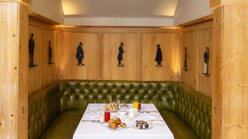 A dining area with a green upholstered bench, a white table set for two, and wooden paneling with figurines on the walls.