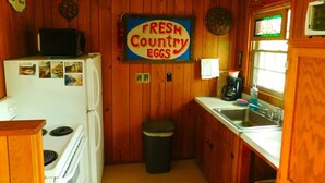 A kitchen with wooden walls, a stove, a refrigerator, a sink, and a 'Fresh Country Eggs' sign. - Rock Eddy Bluff Farm (Dixon)