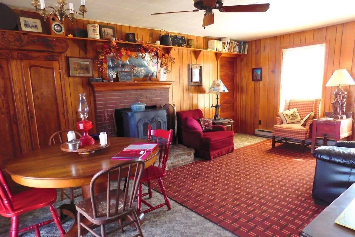 Un interior de madera con una mesa de comedor, sillas rojas, una chimenea y una alfombra roja con estampado.