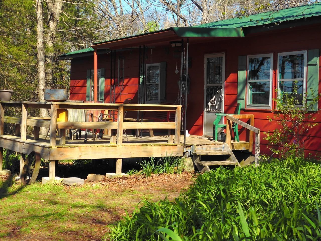 A red cabin with a wooden deck, a green door, and a window.