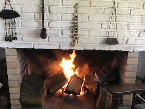 A fireplace with a white brick surround, logs burning, and hanging decorations. - Verde Verde (Punta del Este)
