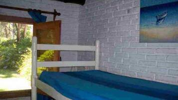 A bunk bed with a blue mattress in a room with white brick walls and a painting of a boat on the wall.