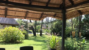 A covered outdoor area with a thatched roof, surrounded by lush greenery and trees. - Verde Verde (Punta del Este)
