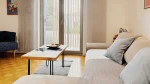 Una sala de estar con un sofá, una mesa de centro y un sillón. Hay un ventanal corredero que da a un balcón.