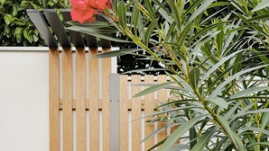 Una puerta de madera con un cabezal de ducha, un cartel que indica lavar la arena en la ducha exterior antes de entrar al apartamento, y una planta verde exuberante en primer plano.