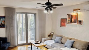 Sala de estar con sofá, una mesita de centro y un ventilador de techo. Cuenta con una puerta corrediza de vidrio que da a un espacio exterior.