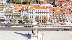 A plaza with a central monument, surrounded by buildings with red-tiled roofs. - The Rossio Studio (Lisboa ciudad)