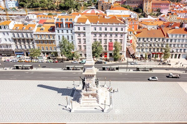 A city square with a central monument, surrounded by historic buildings with red-tiled roofs.