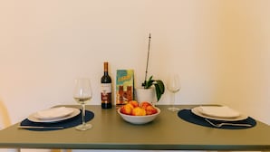 A dining table set with two plates, two wine glasses, a bottle of wine, a bowl of fruit, a book, and a potted plant. - The Rossio Studio (Lisboa ciudad)