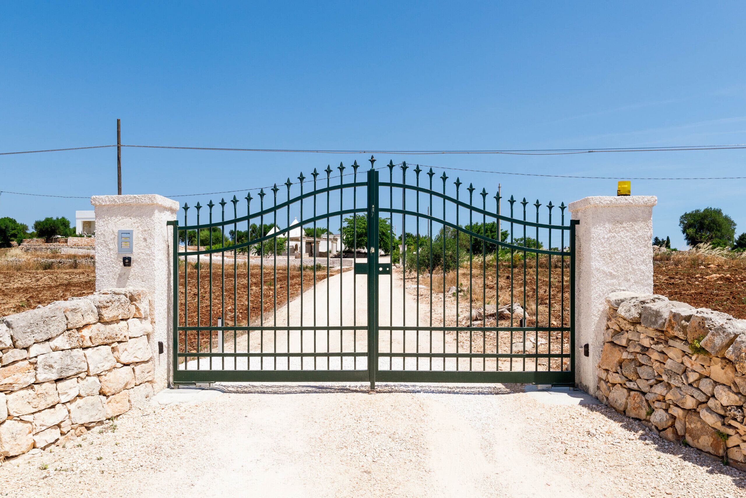 A gated entrance with a stone wall and a metal gate.
