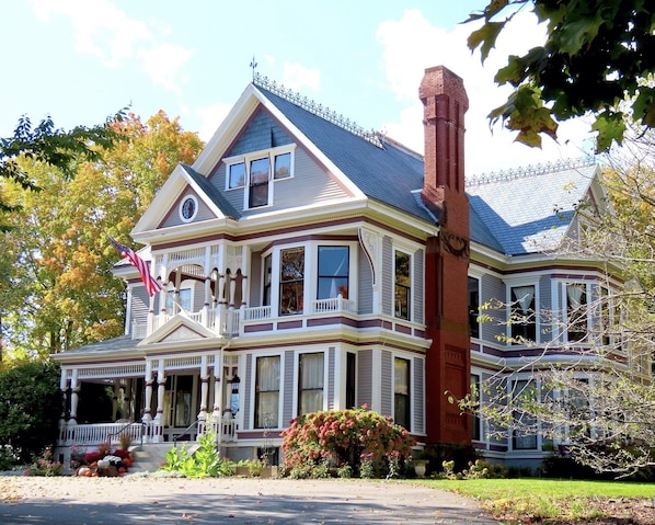 Stately Victorian home with a wrap-around porch and large windows, set amidst mature trees and a well-manicured lawn.