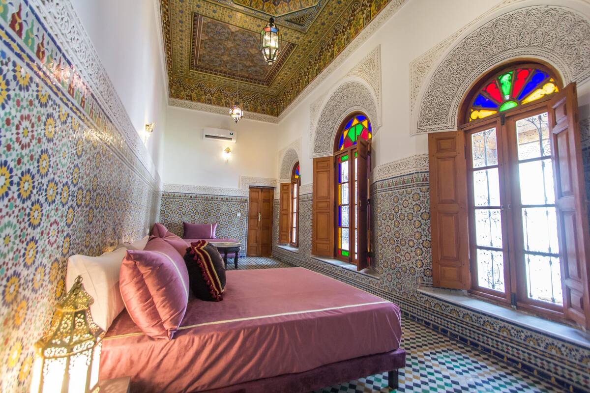 Une chambre dotée d’un grand lit, d’un plafond richement décoré et de vitraux colorés.