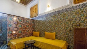 Una habitación con un sofá amarillo, una pequeña mesa redonda y una pared de azulejos estampados.
