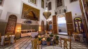 Un interior tradicional con arcos ornamentales, una araña y una zona de estar con mesas y sillas.