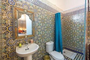 Ein Badezimmer mit Wand aus Mosaikfliesen, einem Waschbecken, einer Toilette und einer Dusche mit blauer Duschvorhang.