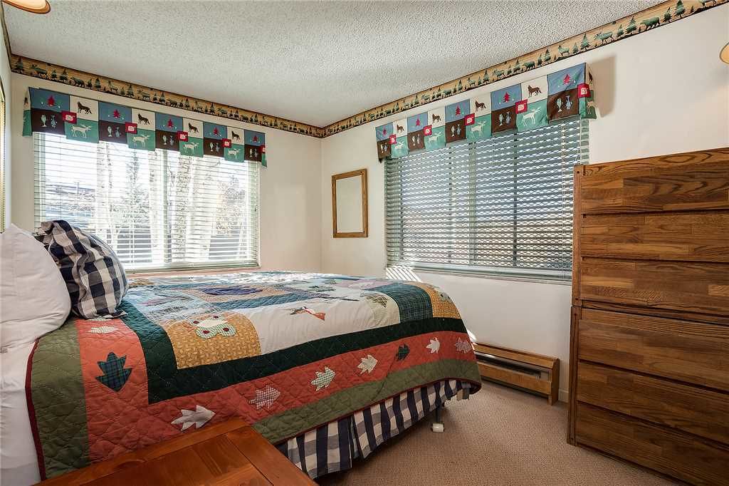 Ett sovrum med en säng, en byrå och ett fönster med persienner.