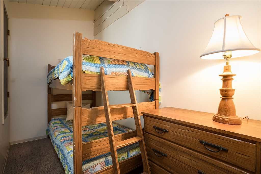 A bunk bed with a ladder, a wooden desk with drawers, and a table lamp.