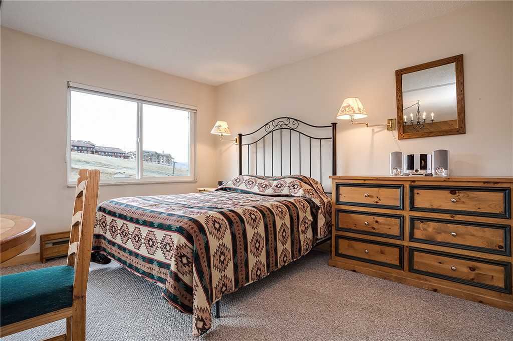 A bedroom with a bed, a dresser, a chair, a window, and a lamp.