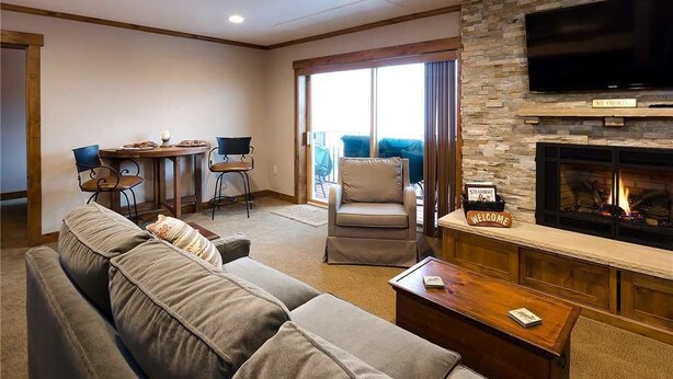 A living room with a fireplace, a sofa, a television, and a dining area with chairs. - Storm Meadows 300-400 at Christie Base (Steamboat Springs)