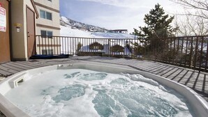 A hot tub on a wooden deck with a view of a snowy mountain and a building in the background. - Storm Meadows 300-400 at Christie Base (Steamboat Springs)