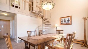 A dining area with a wooden table and chairs, a spiral staircase, and a framed picture on the wall. - Storm Meadows 300-400 at Christie Base (Steamboat Springs)