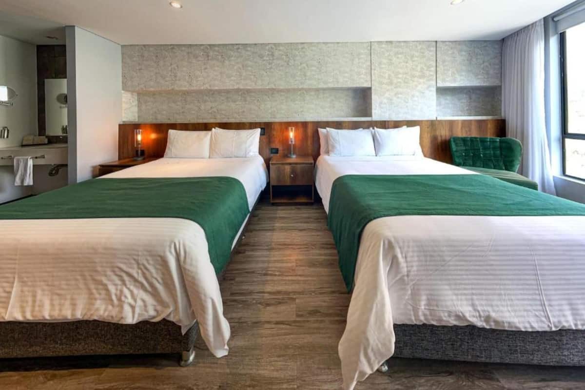 A hotel room with two beds, a wooden floor, a large window, and a stone wall.