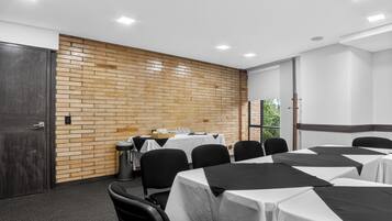Una sala de conferencias con pared de ladrillo, mesas blancas, sillas negras y una puerta.