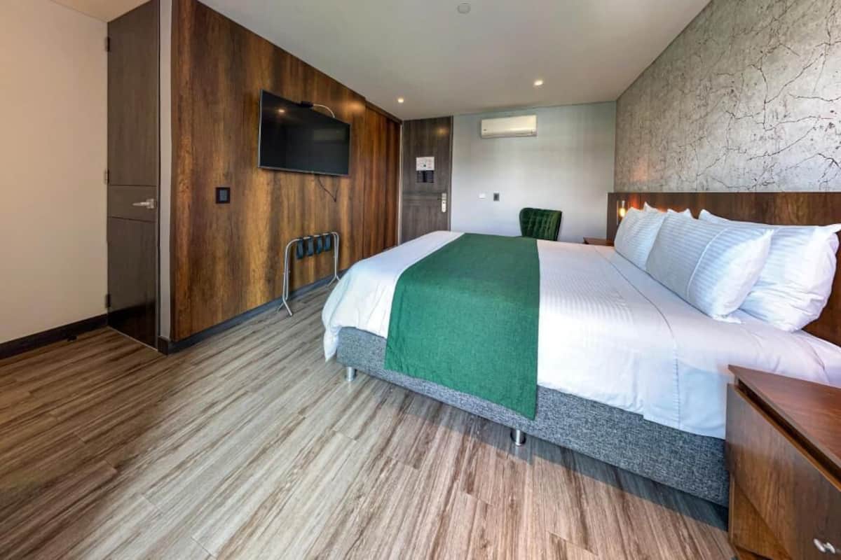 A hotel room with a bed, a television, a wardrobe, and a wall-mounted air conditioner.