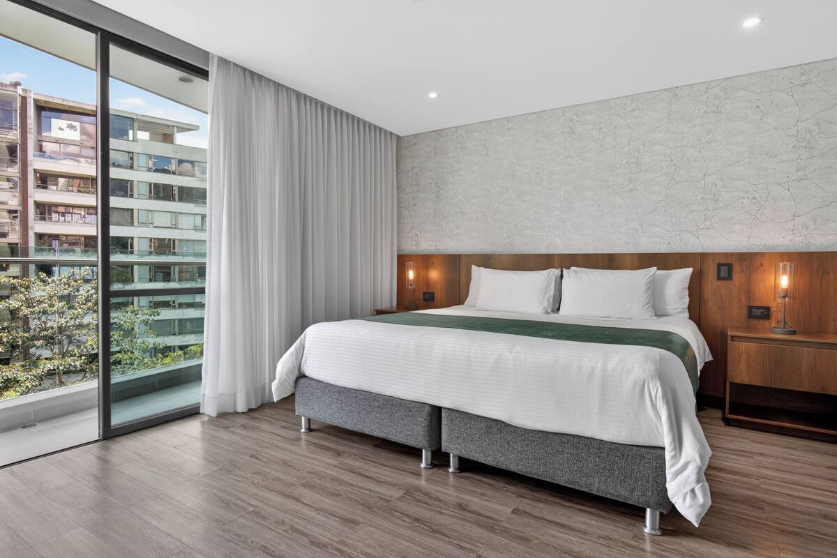 A modern hotel room with a large bed, a view of the city, and a balcony.