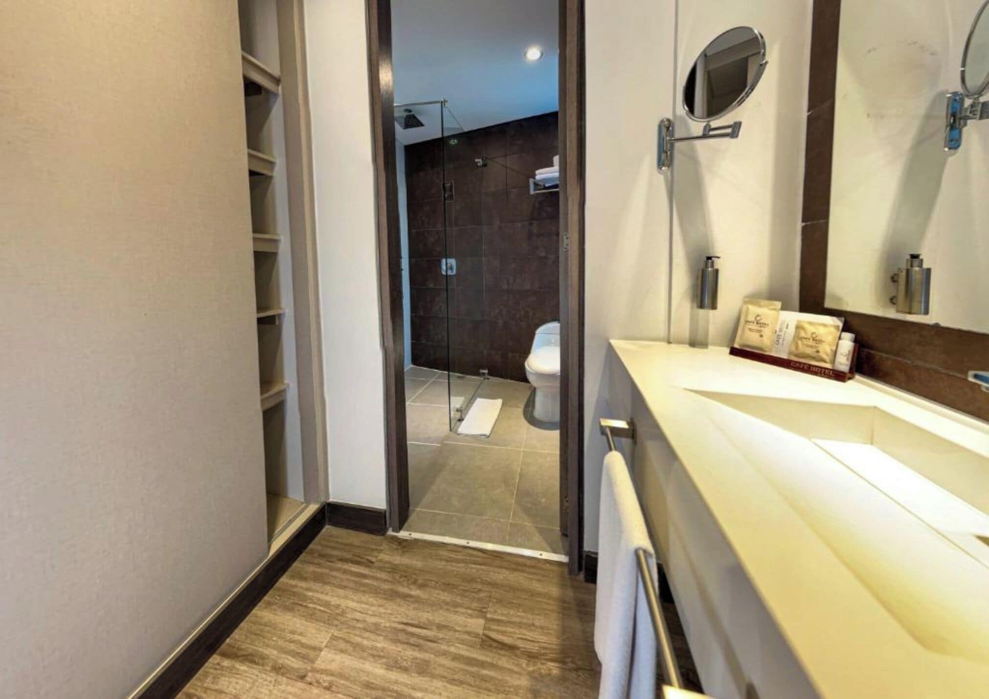 A modern bathroom with a wooden floor, a white sink, a mirror, and a glass shower enclosure.