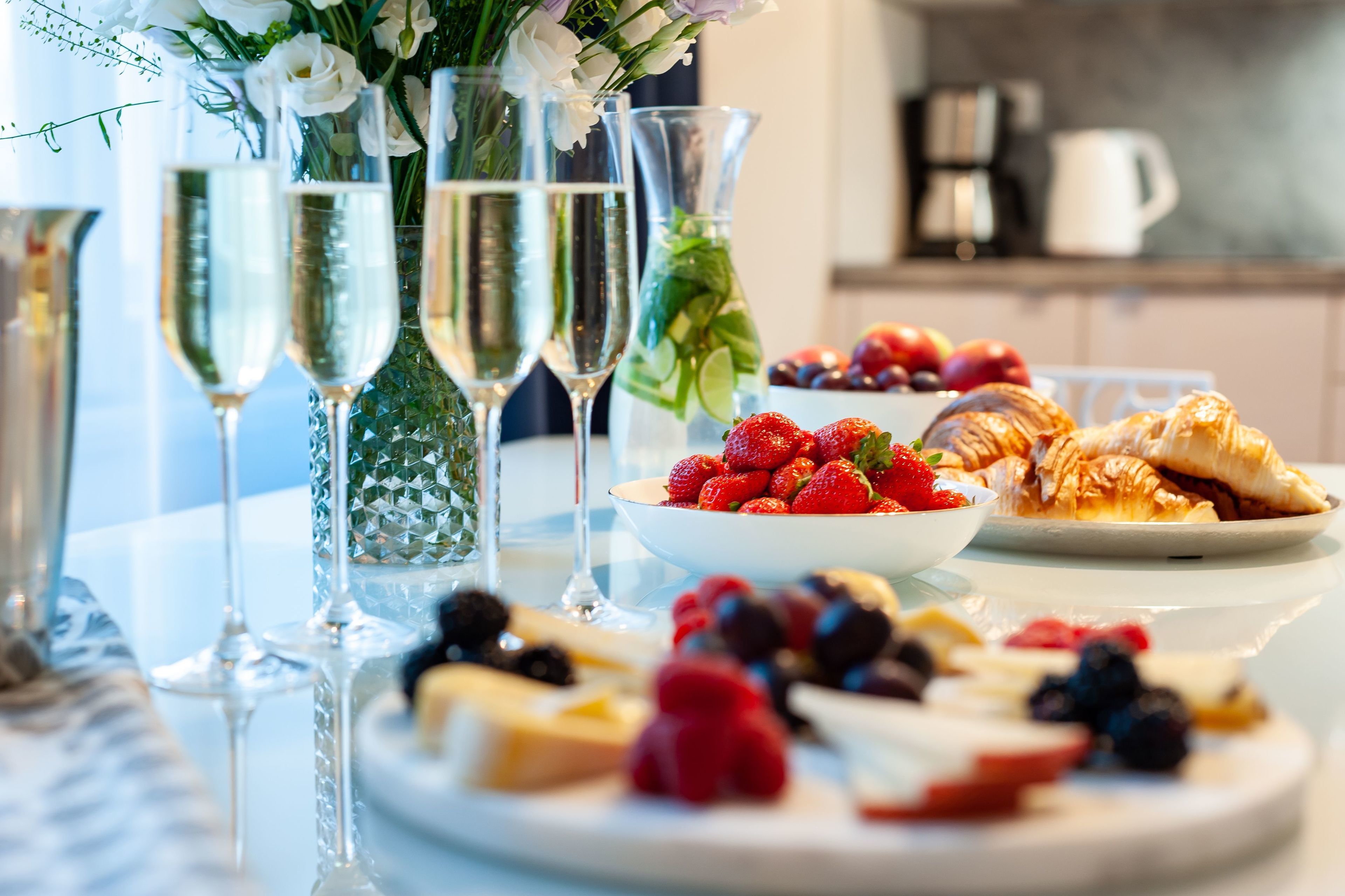 A table with champagne flutes, a bowl of strawberries, and a plate of pastries.