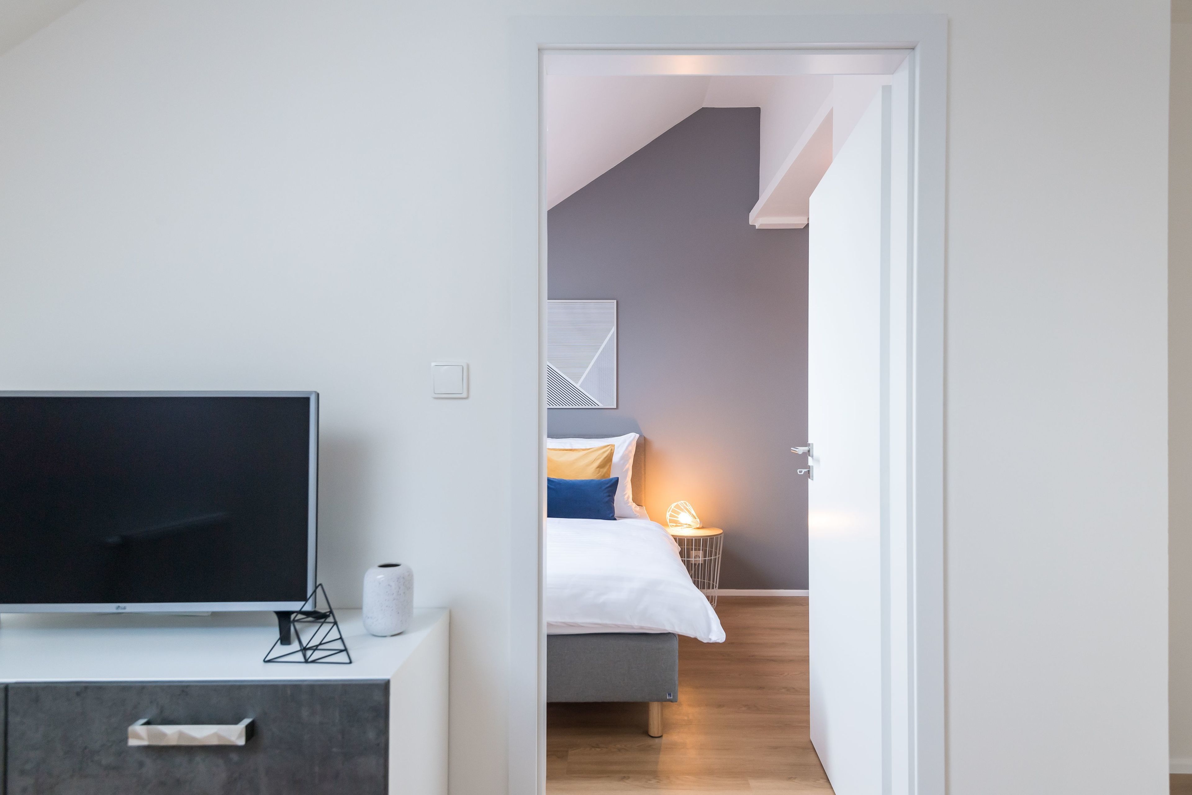 Een moderne hotelkamer met een flatscreen-tv, een nachtkastje met een vaas, en een bed met hoofdeinde.