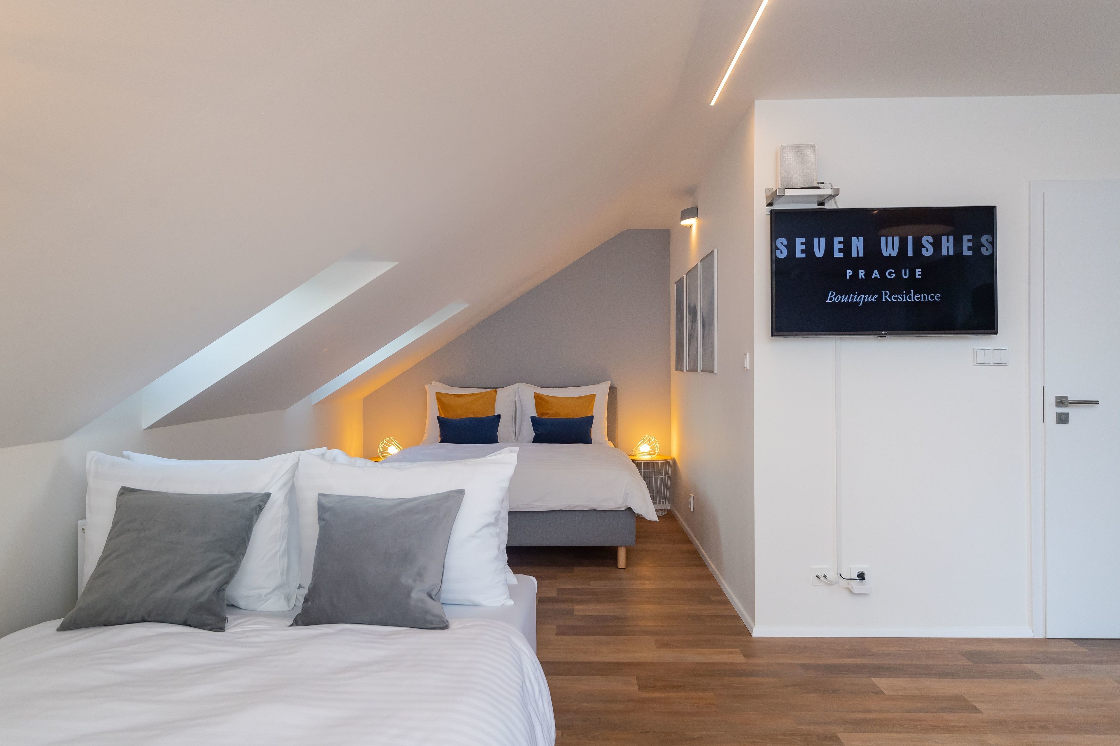 Een slaapkamer met twee bedden, een televisie en een bordje met de tekst 'SEVEN WISHES PRAGUE Boutique Residence'.