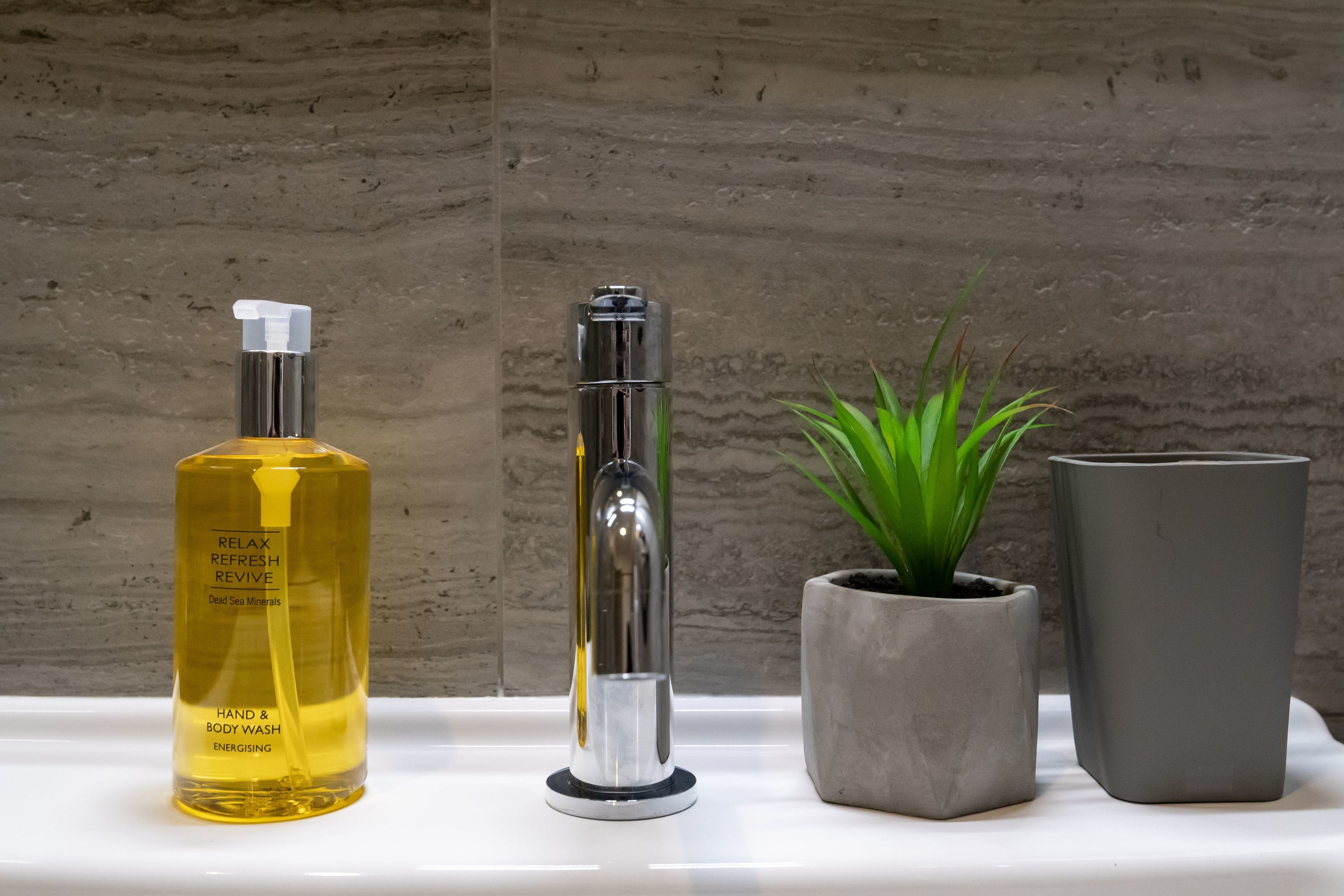 Una encimera de baño con una botella de jabón de manos y cuerpo, un cabezal de ducha y dos plantas en macetas.