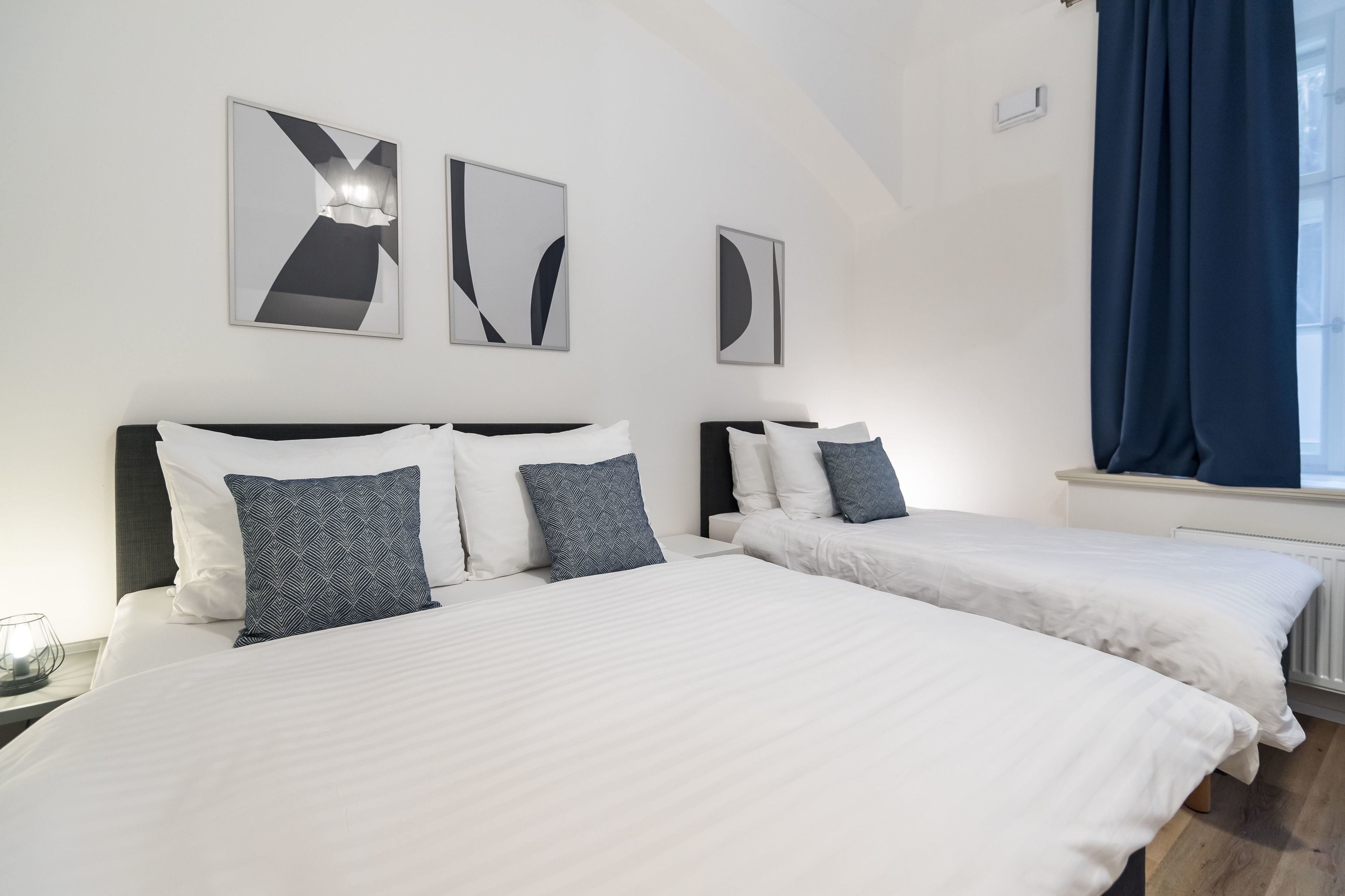 Une chambre d’hôtel avec deux lits, du linge de lit blanc et des œuvres d’art abstraites accrochées aux murs.