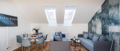 A modern living room with a dining area, featuring a sofa, a coffee table, a dining table with chairs, and a TV mounted on the wall.