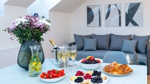 Een eettafel met bloemen, champagne, glazen en diverse soorten fruit en gebak.