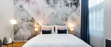 A modern bedroom with a large bed, geometric wall art, and bedside lamps.