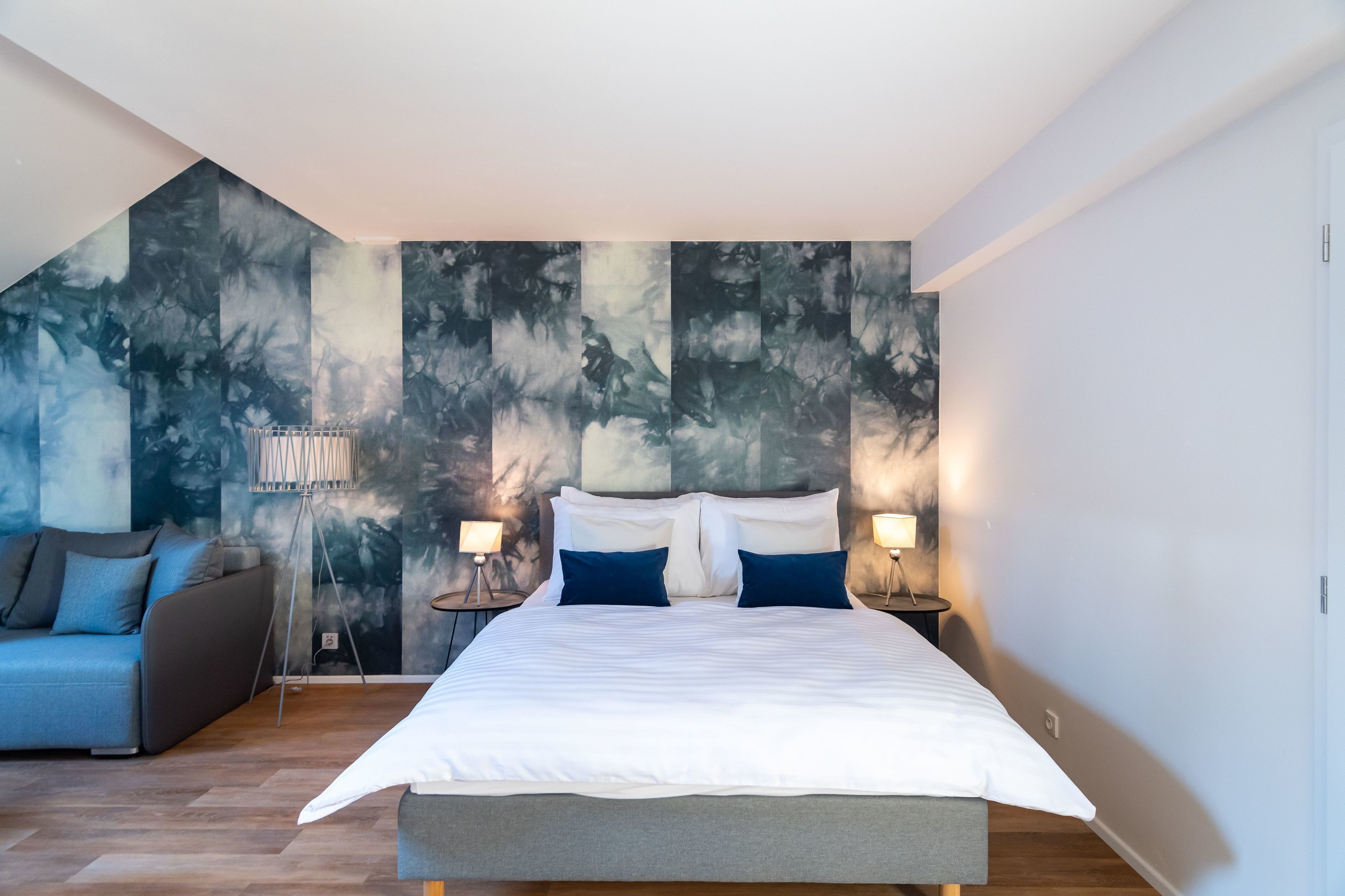 A modern bedroom with a large bed, a sofa, and a unique abstract wall mural.