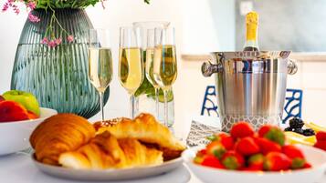 A table with a bottle of champagne, three glasses of champagne, a vase with flowers, a plate of croissants, and a bowl of strawberries.